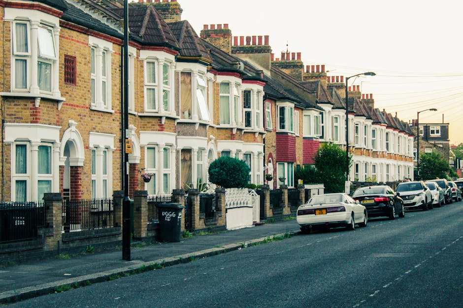 A quiet residential street in Highbury lined with parked cars on both sides, including sedans, hatchbacks, and commercial vans, some of which display branding or are covered with protective materials.